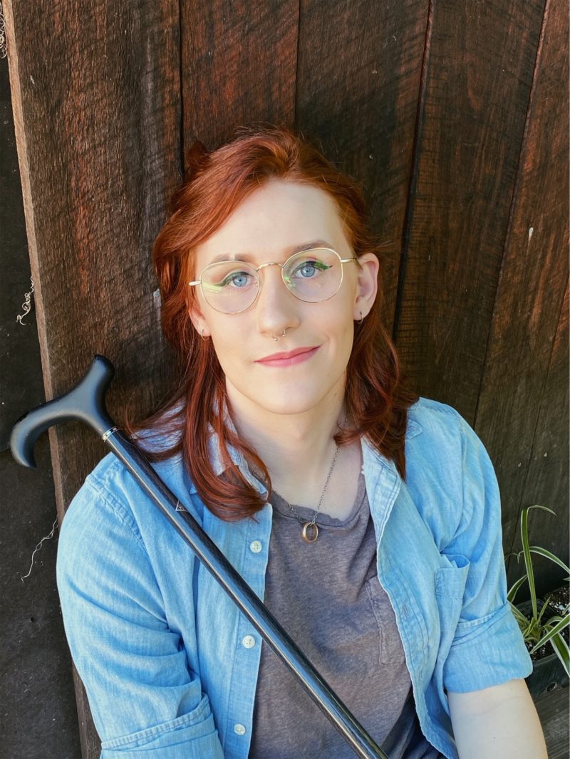 Red headed woman with circular glasses looking at the camera holding a cane